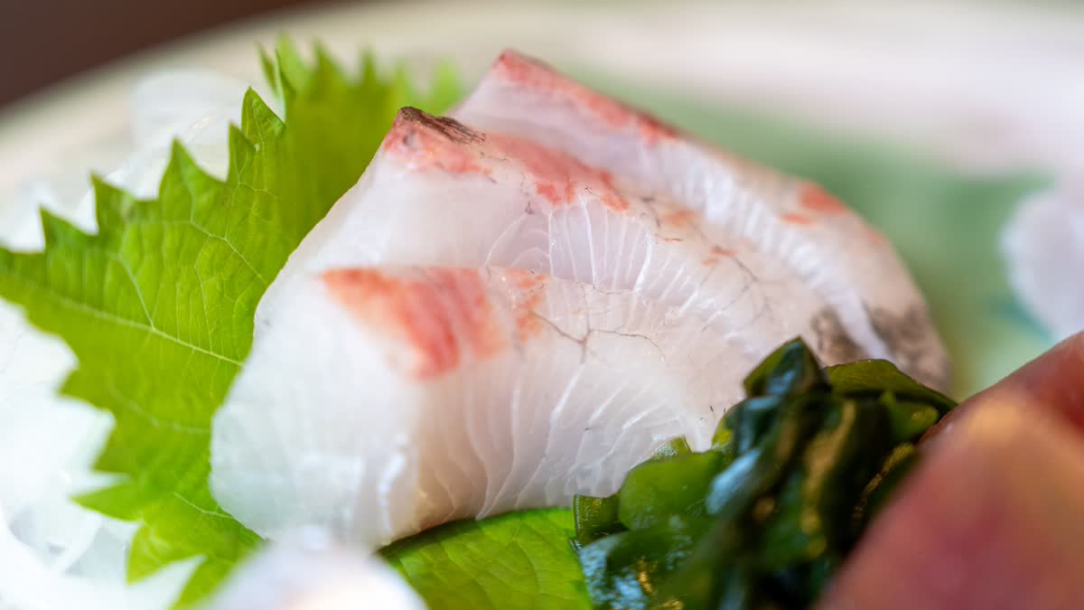 皮目に軽く炙りを入れた白身魚の刺身を大葉とわかめとともにクローズアップで撮影した写真